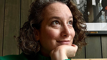 Marie Turner, a middle-aged white woman with curly hair wearing a green sweater, poses looking to the right of the frame and lightly smiling.