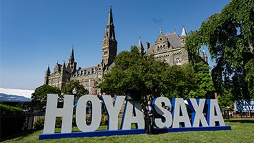 Healy Hall with an oversized "Hoya Saxa" sign in front of it on a clear, sunny day.