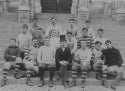 Black and white photograph of the Football team on the steps of Healy Hall, pictured before the traditional Thanksgiving football game, November 24, 1892. the coach and sixteen team members are pictured.