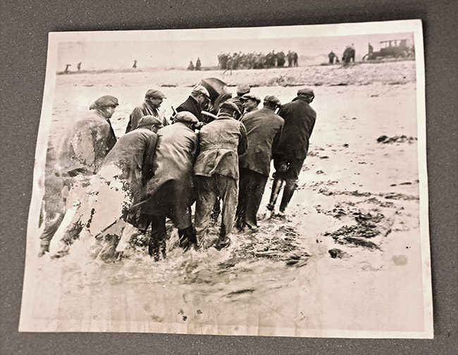 photograph of fishermen carrying an airplane engine from the sea onto shore after conservation treatment