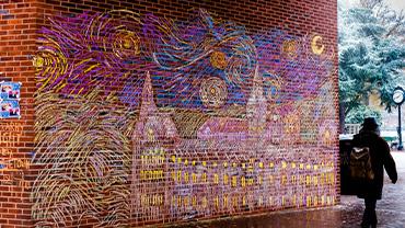 An elaborate chalk mural on Georgetown's Red Square depicts Healy Hall in the style of Van Gogh's "The Starry Night", with a girl walking by the mural on a cloudy day.