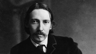 A black and white photograph of writer Robert Louis Stevenson, a young white man with a moustache sitting in front of a simple backdrop.