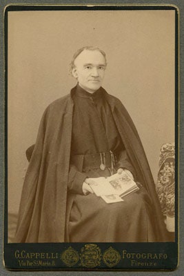 Very Reverend Anton Maria Anderledy, S.J., seated in his cossack with an open book in his lap, with the name of the photography studio G. Cappelli Fotografo printed below the photo