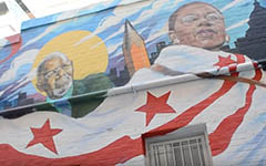 Mural on a building showing people behind a waving D.C. flag, in a screen cap from the Downloading Statehood video