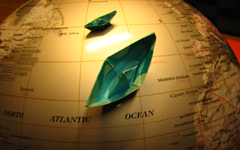 Green origami boats floating on the sea of a globe.
