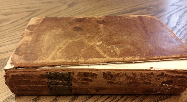 image of a book lying flat on a table with the book spine facing the viewer and with the upper cover detaching and the leather covering flaking away
