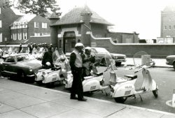 Black and white photograph of policemen wearing gas masks with their scooters across the street from the Prospect Street entrance to the Car Barn