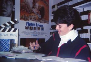 Image of Corp member Jen McAle looking down at her work while in Movie Mayhem. Several movie posters and VHS cases are visible behind her.