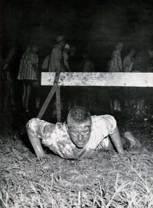 Black and white photograph of a new student crawling through mud as part of hazing.