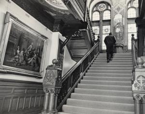 Black and white photograph taken from the lobby of Healy Hall showing Jason Miller walking up the stairs