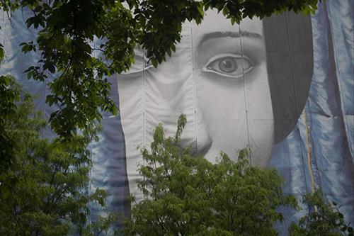 Wall with a face painted on it looking through overhanging trees. 