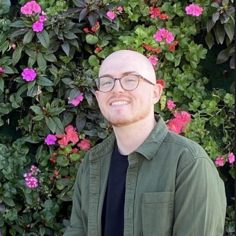 Joe Gurr smiles at the camera in front of a wall of blooming begonias and geraniums