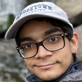 Umar Ahmed Badami wears a puffy coat and a Georgetown ball cap with a waterfall in the background