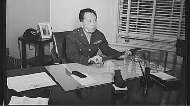 Black and white photography of a Filipino man in a military uniform sitting behind a large office desk