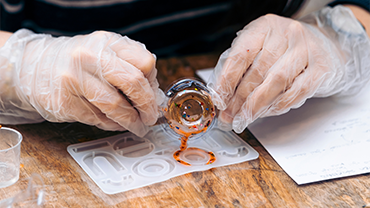 two hands with gloves on carefully pouring resin into a ring mold